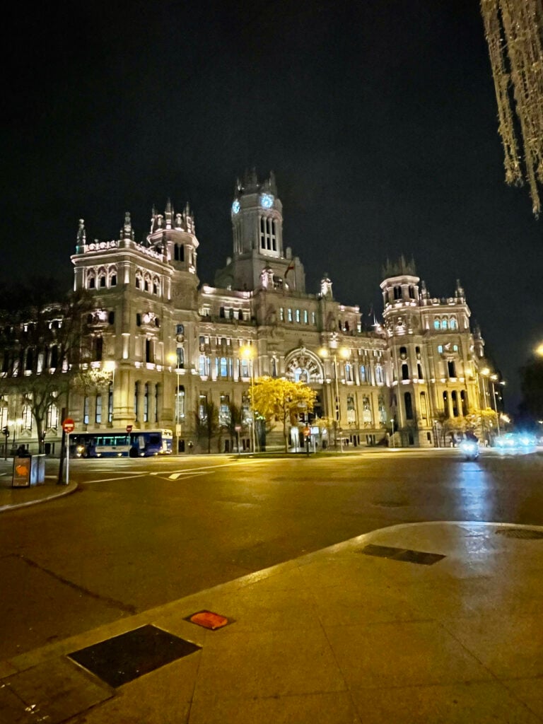 Cibeles Palace illuminated at night in Madrid with city lights and traffic in the foreground.