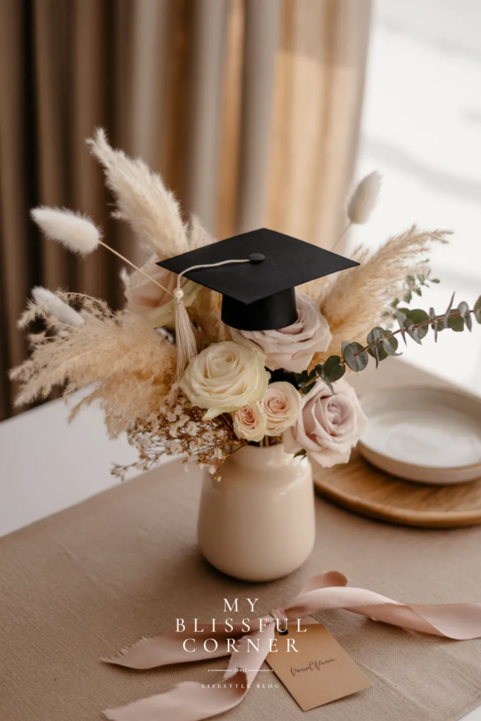 Elegant graduation centerpiece with pampas grass, blush roses, greenery, and a graduation cap in a neutral vase