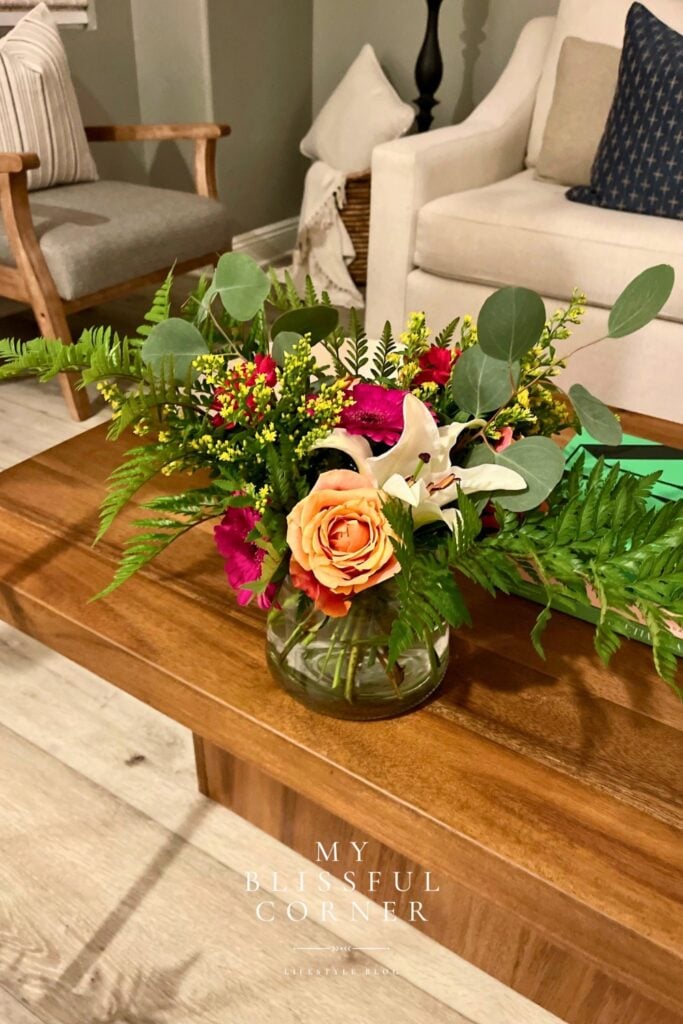 DIY tropical flower centerpiece in glass vase with roses lilies ferns and eucalyptus