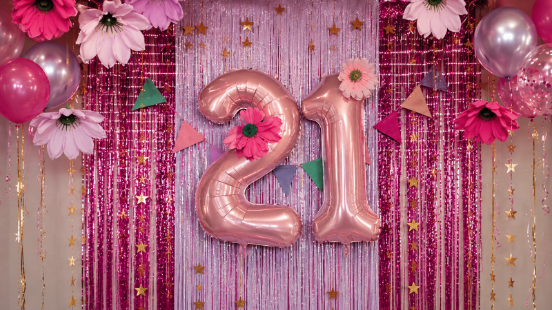 Pink and rose gold 21st birthday party backdrop with rose gold number balloons and festive decorations.