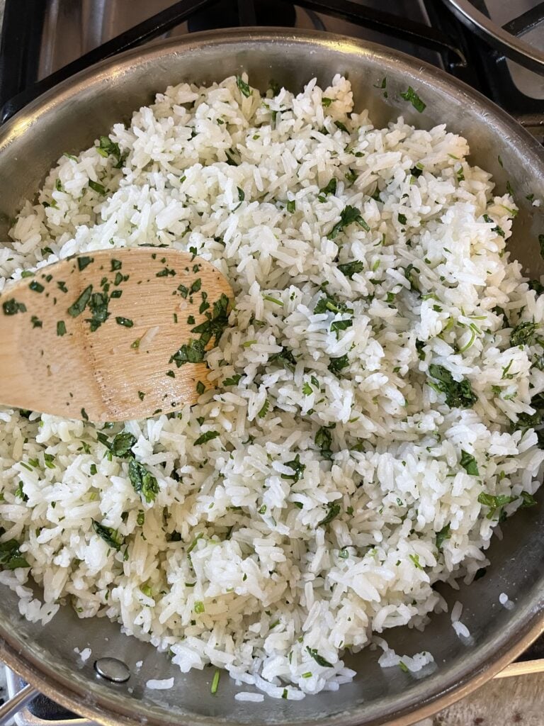 Chipotle-style cilantro lime rice being stirred in a skillet with fresh cilantro and lime juice for an easy copycat recipe.
