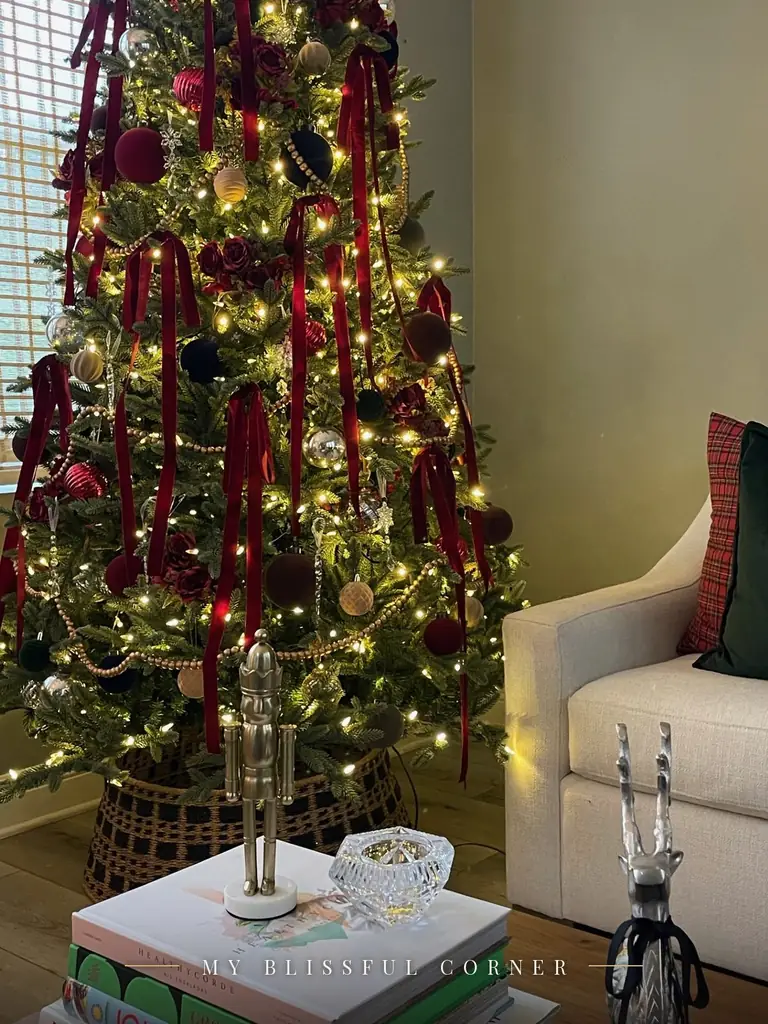 Close-up of a Ralph Lauren Christmas tree with velvet ornaments, a woven tree collar, and a brass nutcracker on a stack of books